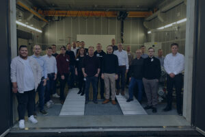 Gruppenbild des Projektkonsortiums von DigiPrüF vor dem Fahrzeugprüfstand der Hochschule Aalen als Titelbild des Blogartikels